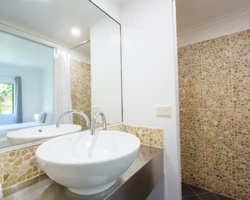 Bathroom with walk-in shower and basin in a 1 or 2 bedroom apartment at Mango Lagoon Resort, Palm Cove Cairns, featuring decorative pebble walls