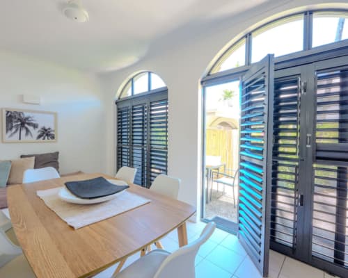 Dining area of a 1 or 2 bedroom courtyard apartment at Mango Lagoon Resort, Palm Cove Cairns, with louvre door open to the courtyard