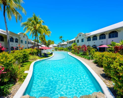 Sparkling pool at Mango Lagoon Resort, Palm Cove Cairns, surrounded by greenery and blue skies, with umbrellas and sun loungers beside the resort accommodation