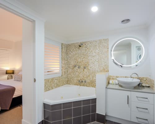 Corner bath/shower in the ensuite of a master bedroom in a 1 or 2 bedroom apartment at Mango Lagoon Resort, Palm Cove Cairns, with decorative pebble walls behind the bath/ shower