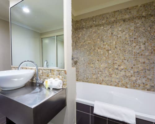 Bathroom with bathtub and basin in a 1 or 2 bedroom apartment at Mango Lagoon Resort, Palm Cove Cairns, featuring decorative pebble walls